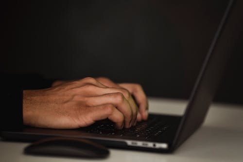 Crop faceless person using laptop in a dark room.