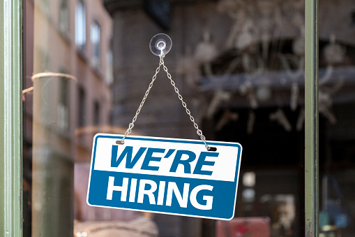 Close-up on a blue and white sign in a window with written in "We're hiring".